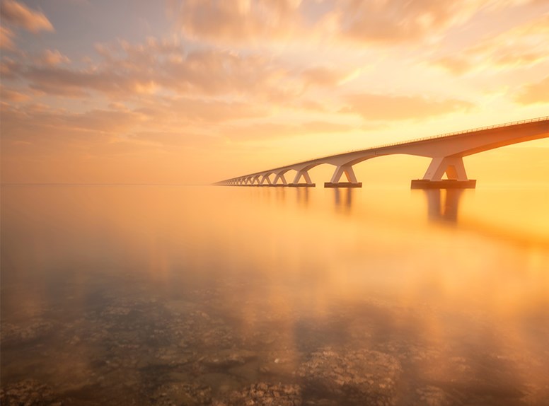 Zeelandbrug tijdens zonsondergang met op de voorgrond de zee