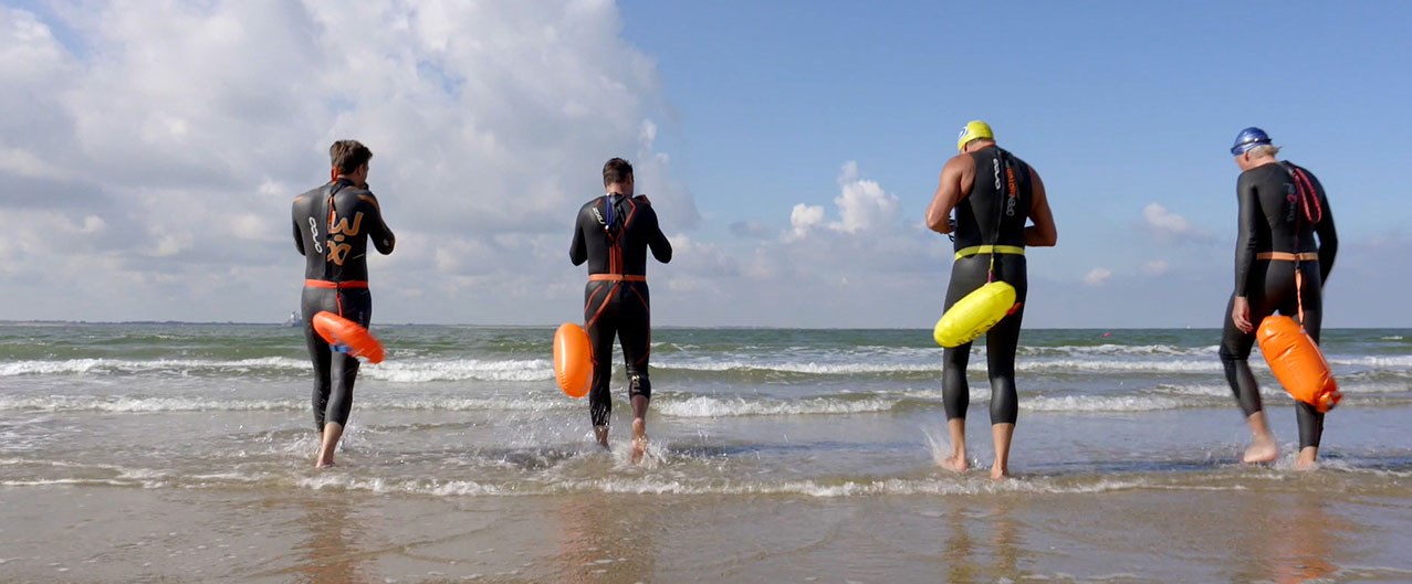 Vier personen met duikpak aan gaan zwemmen aan de zee in Vlissingen